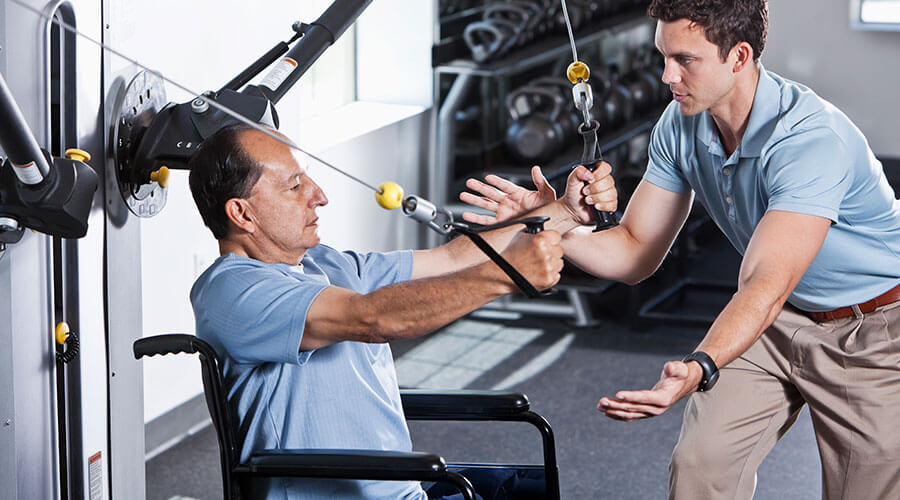 Man in wheel chair receiving therapy from a trainer.
